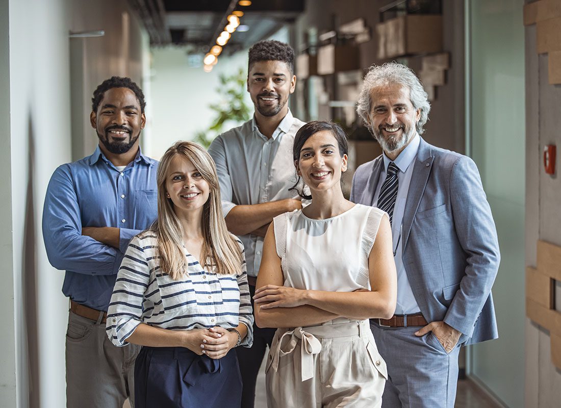 Employee Benefits - Portrait of a Smiling Group of Employees Dressed in Business Casual Attire Standing in the Hallway of an Office