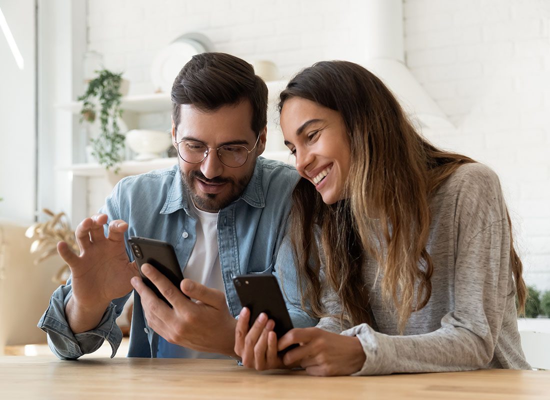 Read Our Reviews - Portrait of a Cheerful Young Couple Sitting in the Dining Room Having Fun Using Their Phones